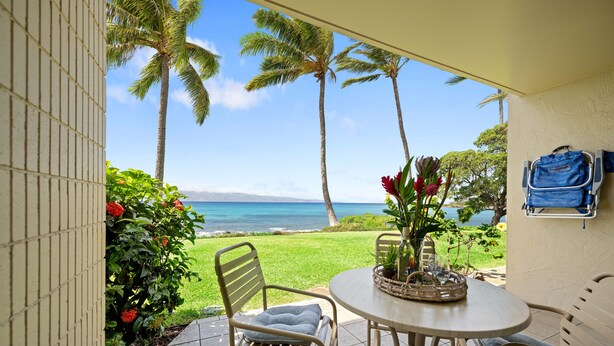 A patio with a view of the ocean, palm trees, and a table with chairs. - Napili Bay beauty, a cozy oceanfront studio (Lahaina)
