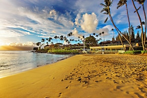 A beach with footprints, palm trees, and a building with a sign. - Napili Bay beauty, a cozy oceanfront studio (Lahaina)