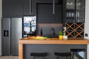 A modern kitchen with a central island, black cabinets, stainless steel appliances, and a wine cabinet.