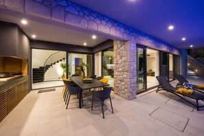 A modern outdoor dining area with a stone wall, a staircase, and a poolside lounge.