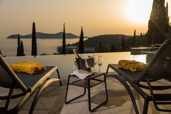 A terrace with two lounge chairs, a table with a bottle of champagne, glasses, and a rolled-up towel.