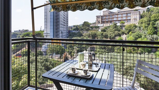 Un balcone con un tavolo apparecchiato per il tè, con vista su una città che include edifici e spazi verdi.