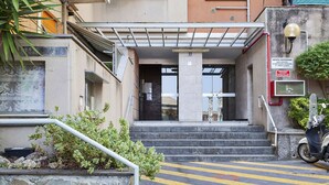 L'ingresso di un edificio con una scalinata coperta, una motocicletta parcheggiata all'esterno e un pulsante di allarme antincendio sulla parete.
