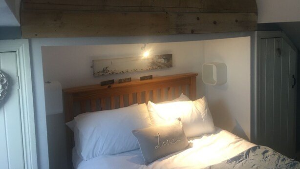 A bedroom with a wooden headboard, a bed with white bedding, and a wall-mounted light fixture. - Driftwood Loft (Downpatrick)