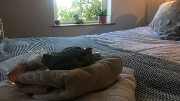 Una cama bien tendida con una colcha azul y blanca a rayas, una almohada verde y una pequeña planta en maceta sobre el alféizar.
