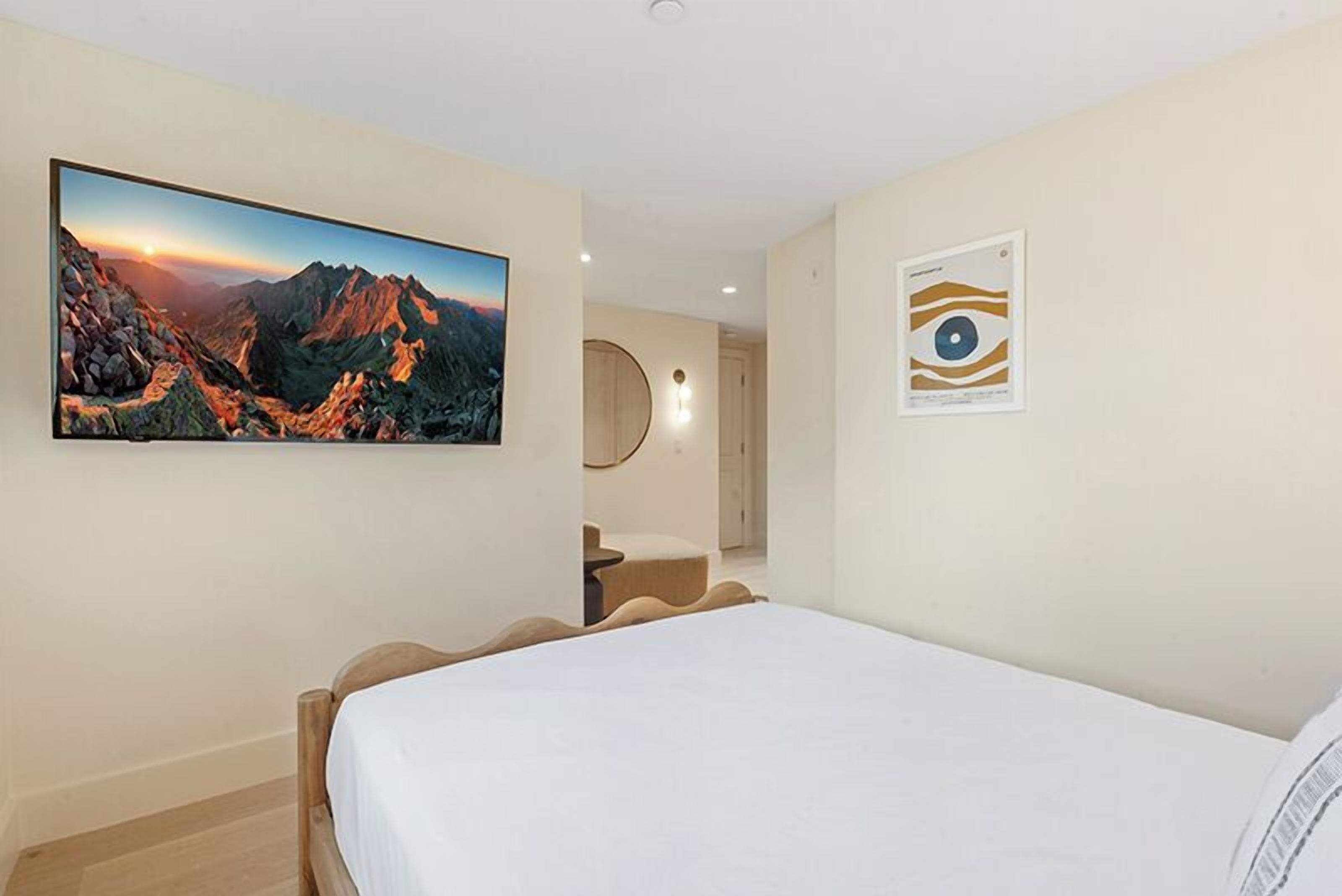 Een slaapkamer met een bed, een schilderij van een berglandschap en een lijst met een foto aan de muur.