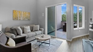 Un salon moderne avec un canapé gris, une table basse et une porte vitrée donnant sur un balcon.