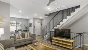 Un salon moderne avec un canapé, une table basse, un téléviseur et un escalier.