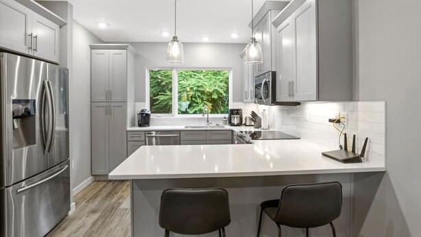 Une cuisine moderne dotée d’appareils électroménagers en acier inoxydable, d’un grand îlot central et de luminaires suspendus.