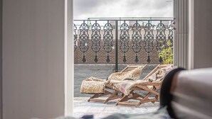 Une chambre avec vue sur un balcon agrémenté de chaises longues et orné d’une grille en fer forgé.