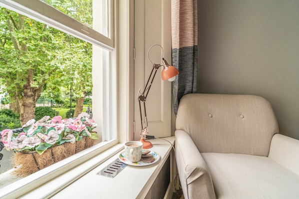 A window seat with a chair, a table, a lamp, and a view of greenery outside. - Georgian House (London)