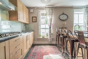 A kitchen with wooden cabinets, a gas stove, and a red patterned rug. - Georgian House (London)