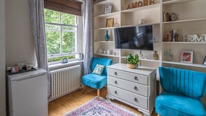 Une pièce confortable avec une grande fenêtre, un radiateur, une télévision et une commode blanche.