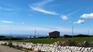 Un paisaje rural con un muro de piedra, un pequeño edificio y un cielo azul despejado.