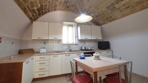 Una cocina compacta con alacenas blancas, estufa, lavamanos y un comedor con mesa y sillas.