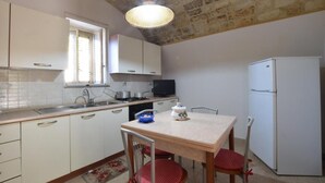 Cocina pequeña con armarios blancos, una mesa de comedor y un refrigerador.