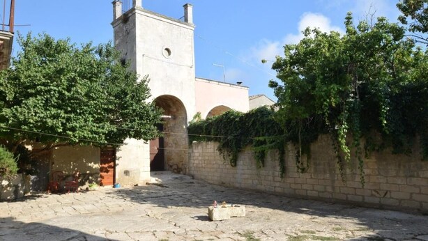 Un patio con suelo de piedra, una torre y un muro cubierto de hiedra.
