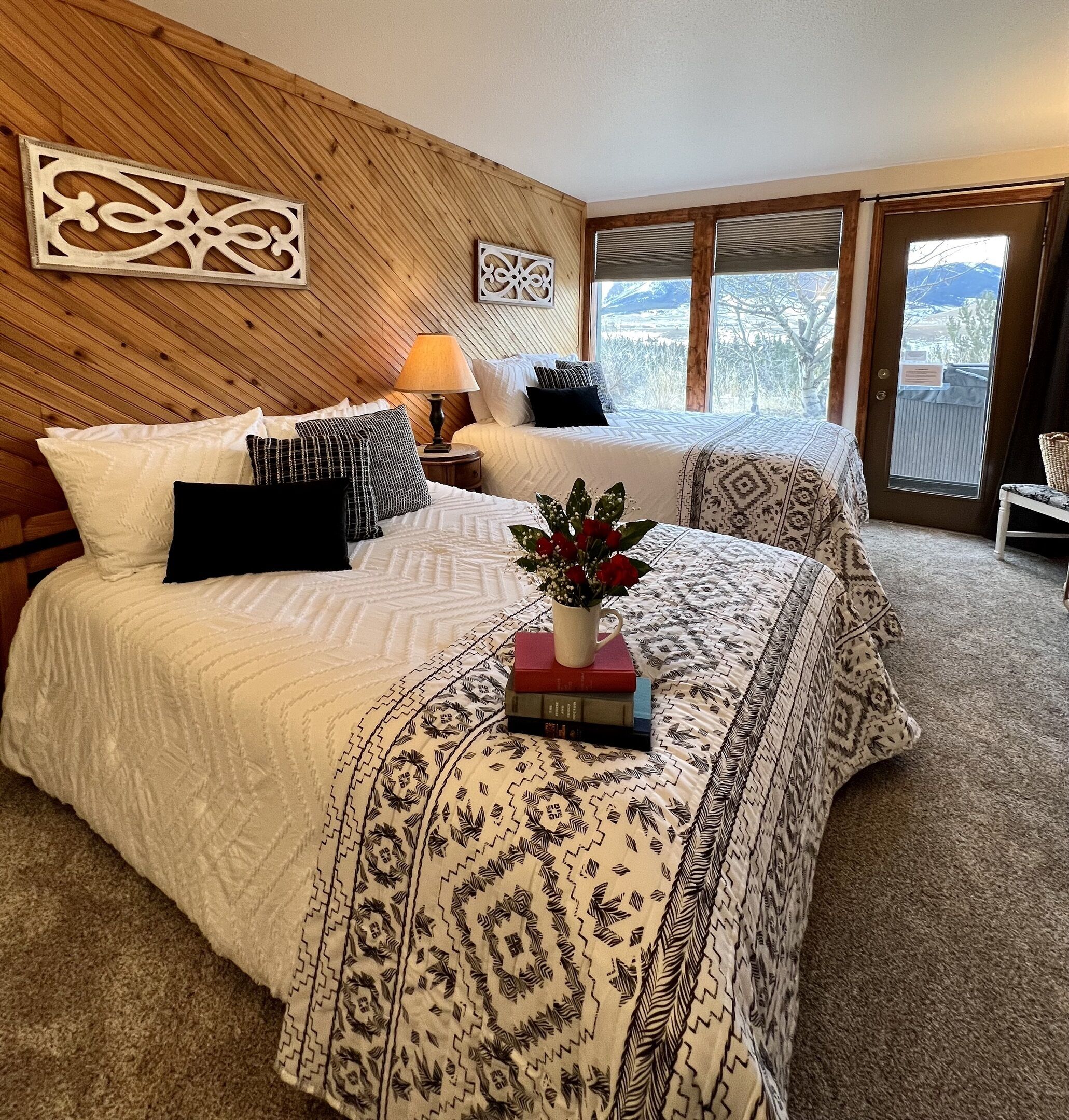 Une chambre avec deux lits, un panneau mural en bois, une fenêtre donnant sur un beau paysage et une plante posée sur l’un des lits.