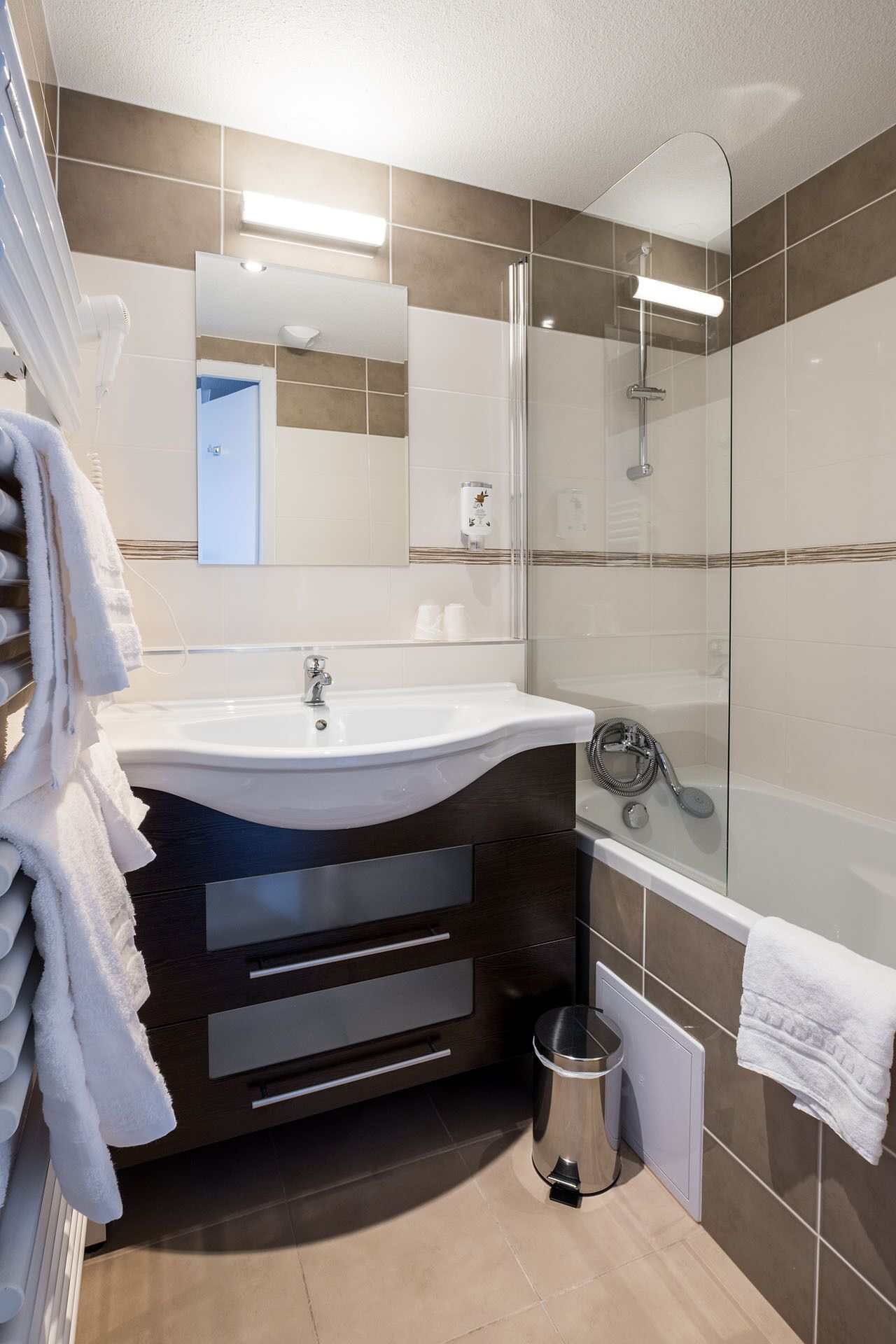 Un baño moderno con un lavamanos blanco, tocador de madera oscura, cabina de ducha de vidrio y un inodoro a la vista.