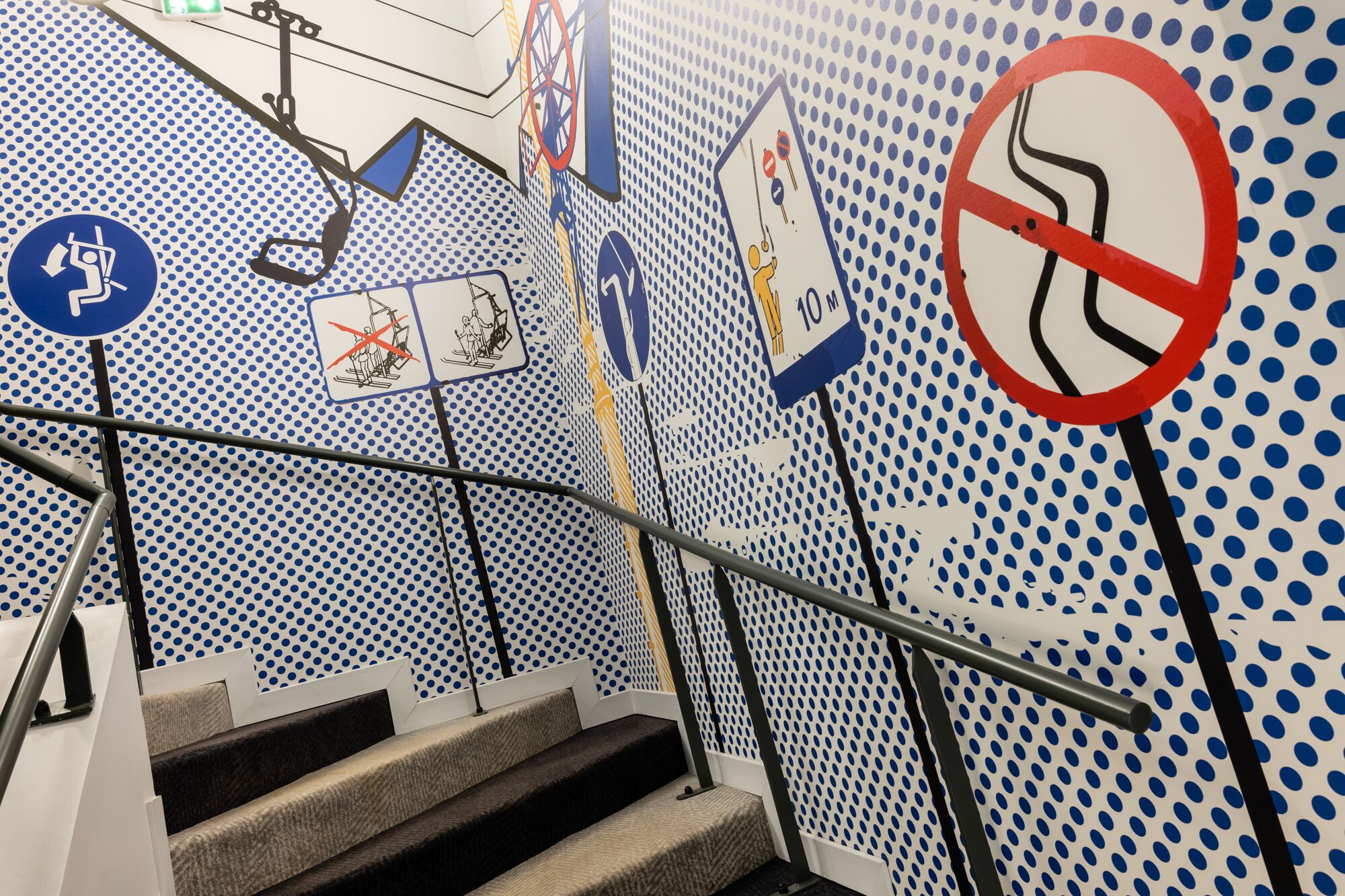 Una escalera con un muro a lunares y varios letreros de seguridad e indicación.