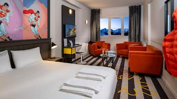 A hotel room with a large bed, two orange armchairs, a small table, and a painting on the wall.