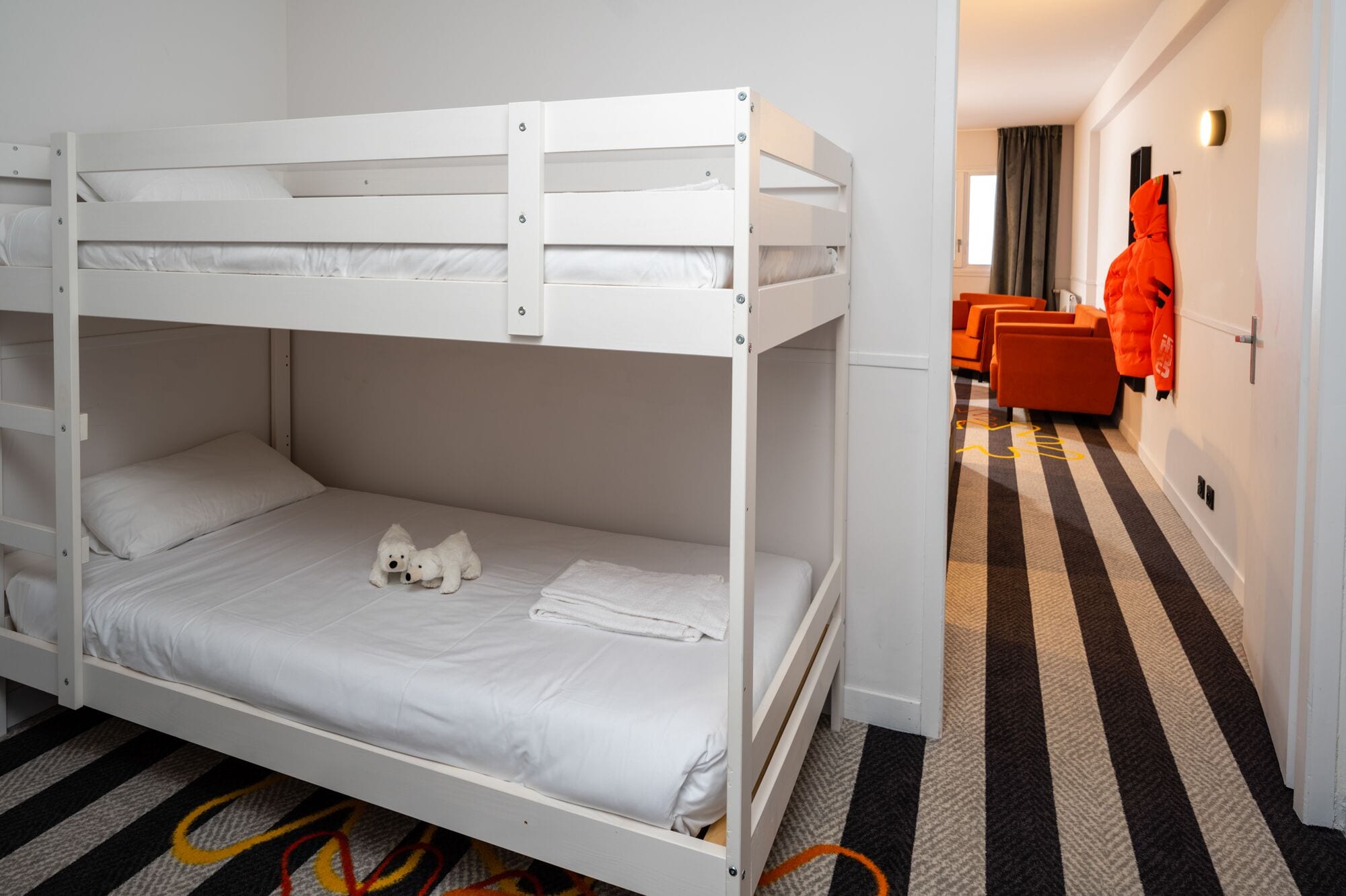 A bunk bed room with white bedding, a pair of stuffed animals, and a striped carpet.