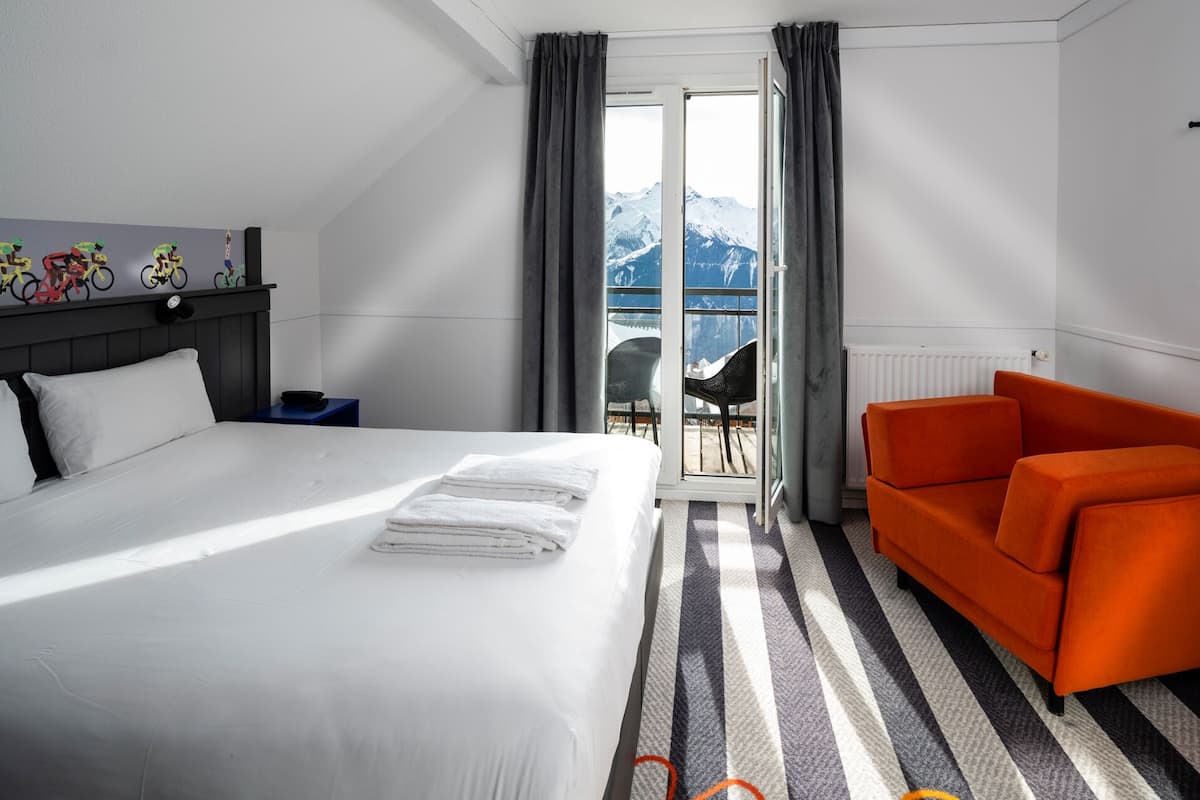 A hotel room with a bed, a sofa, a view of mountains through a window, and a radiator.