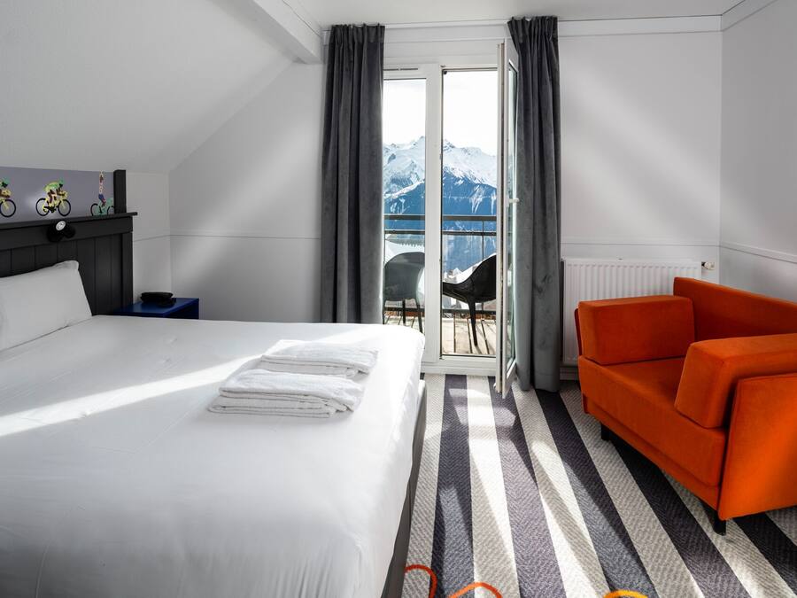 Habitación de hotel con cama, sofá, vistas a las montañas a través de una ventana y un radiador.