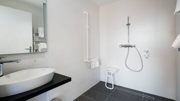 A modern bathroom with a large white sink, a mirror, a shower with a handheld showerhead, and a towel rack.