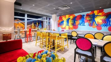 Un restaurante moderno con sillas amarillas y rojas, un mural colorido y vistas a un pueblo nevado a través de amplios ventanales.
