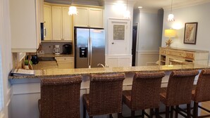Una cocina con una isla central, taburetes de bar, un refrigerador y una cafetera.