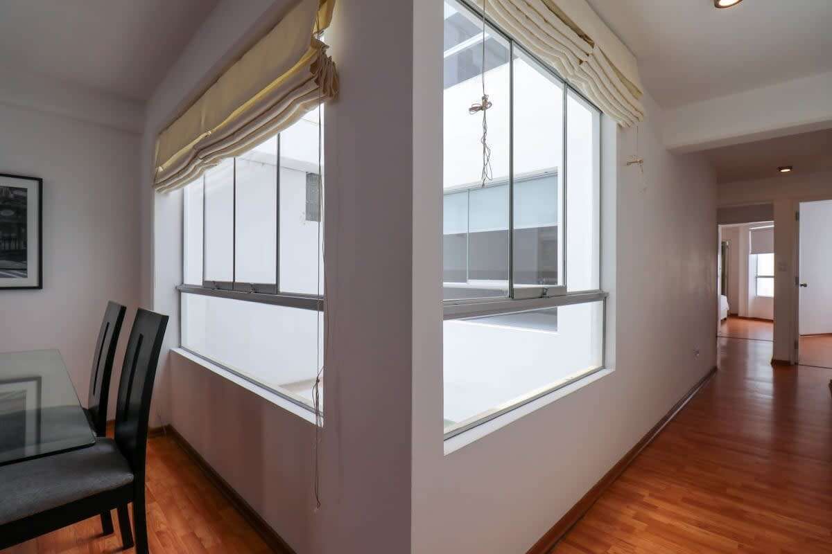 A spacious room with large windows, a dining table with chairs, and a wooden floor.