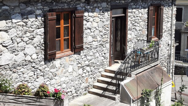 Un bâtiment en pierre avec un toit en pente, des volets en bois et un escalier en métal menant à un balcon.