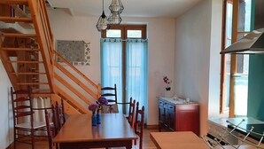 Une cuisine spacieuse avec un plancher en bois, un coin repas avec une table et des chaises en bois, un escalier et une vue sur l’extérieur par une fenêtre.