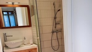 Une salle de bain avec un lavabo blanc, un miroir, une douche avec une porte en verre et des étagères en bois.