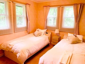 A room with two single beds, a bedside table with a lamp, and windows with blinds.