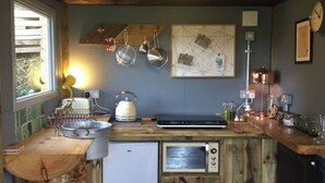 Una cocina rústica con armarios de madera, un refrigerador pequeño, una tetera y diversos utensilios de cocina.