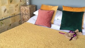 Un dormitorio con cama, almohadas, una mesita de noche e ilustraciones botánicas en la pared.