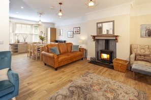 A cozy living room with a fireplace, wooden flooring, and a dining area with a view of the kitchen. - The Dog House, Porlock (Porlock)