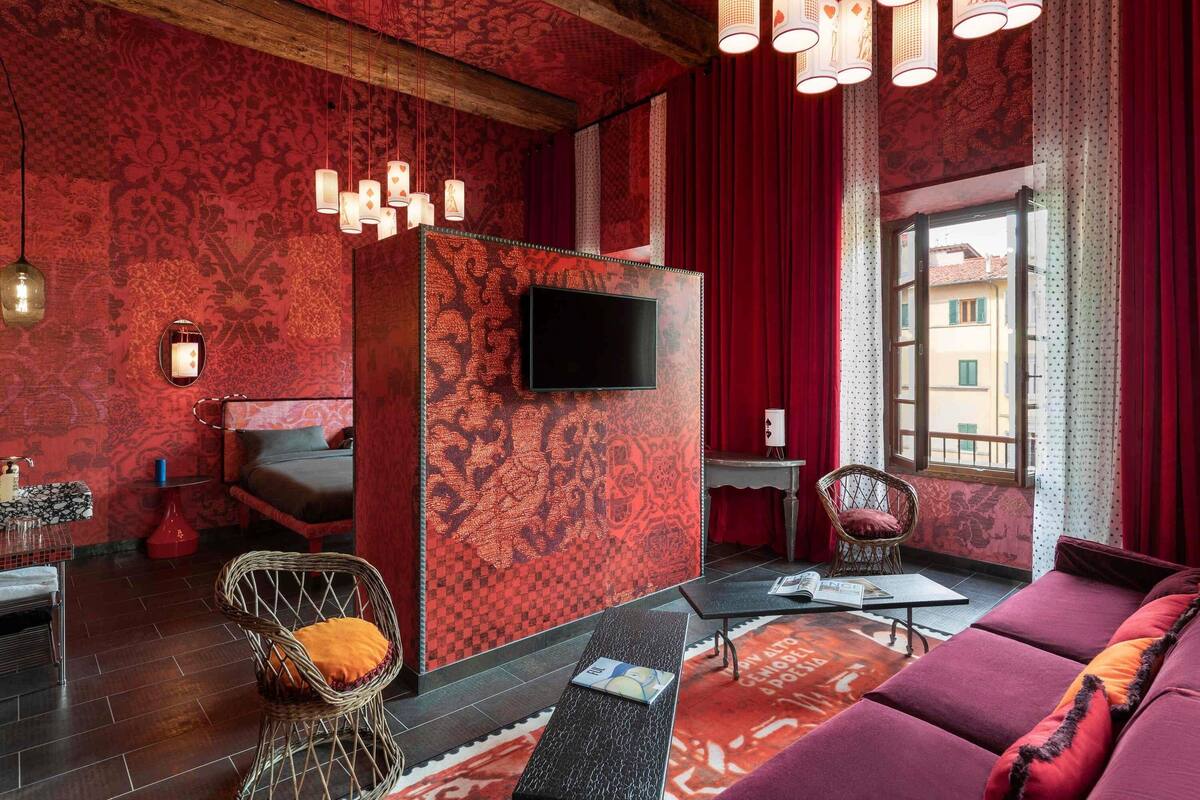 Une pièce avec un mur orné d’un motif rouge, un téléviseur à écran plat, un canapé, un fauteuil en osier et une petite table sur laquelle repose un magazine.