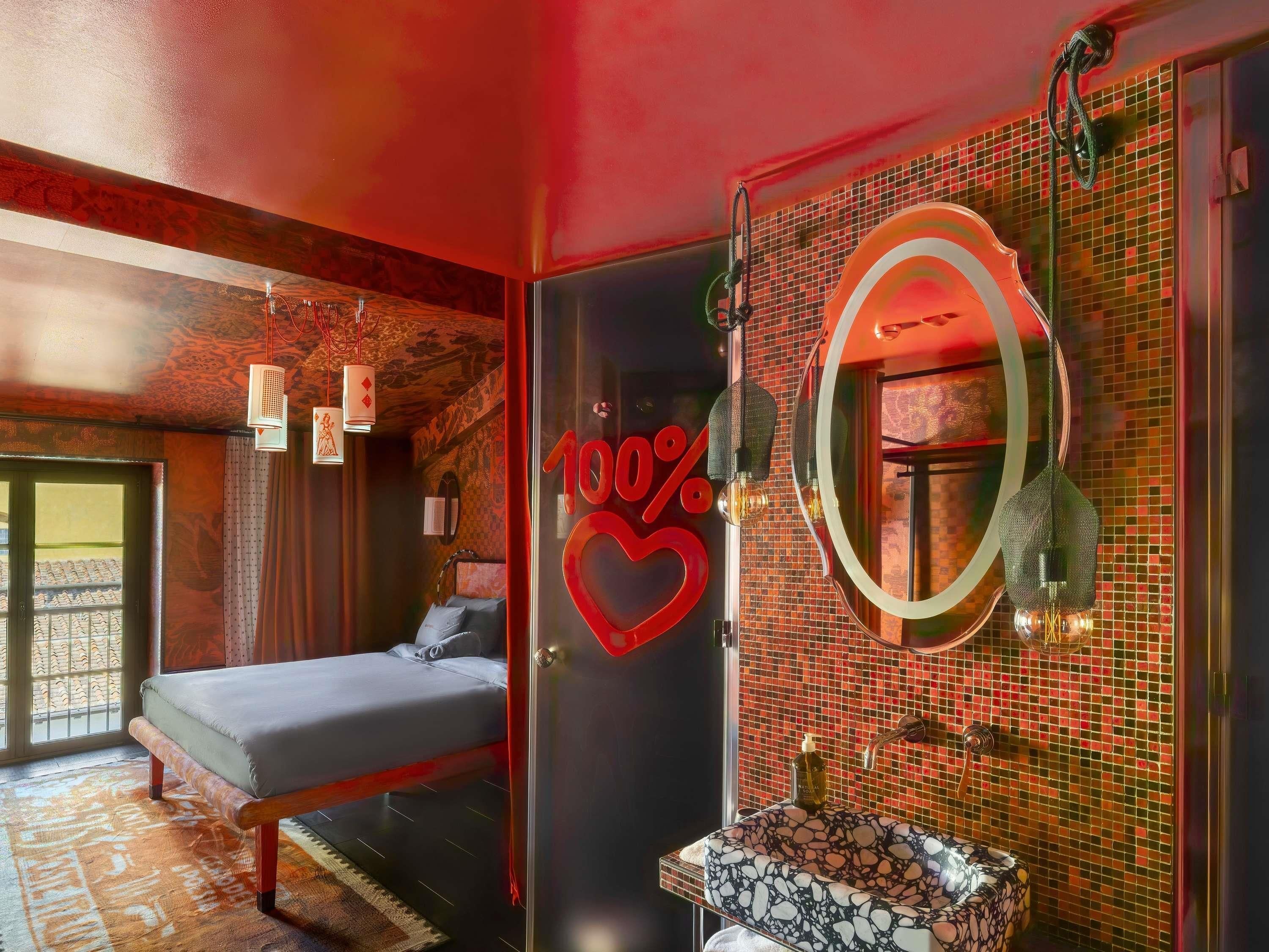Una habitación de hotel con cama, baño con pared de mosaicos y un espejo grande.