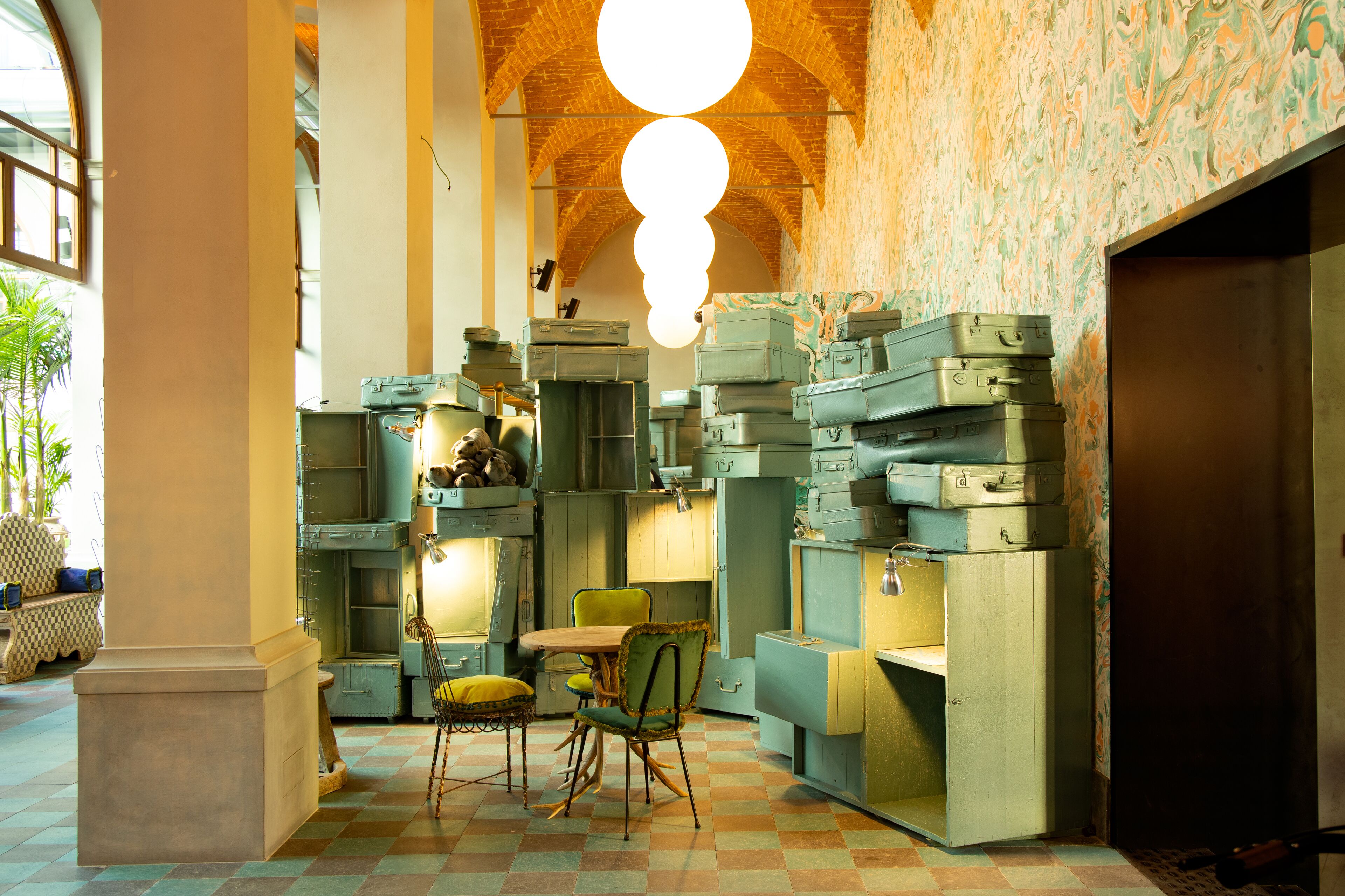Une pièce au style rétro, avec un sol à carreaux, une table en bois entourée de chaises et un mur recouvert de valises empilées.
