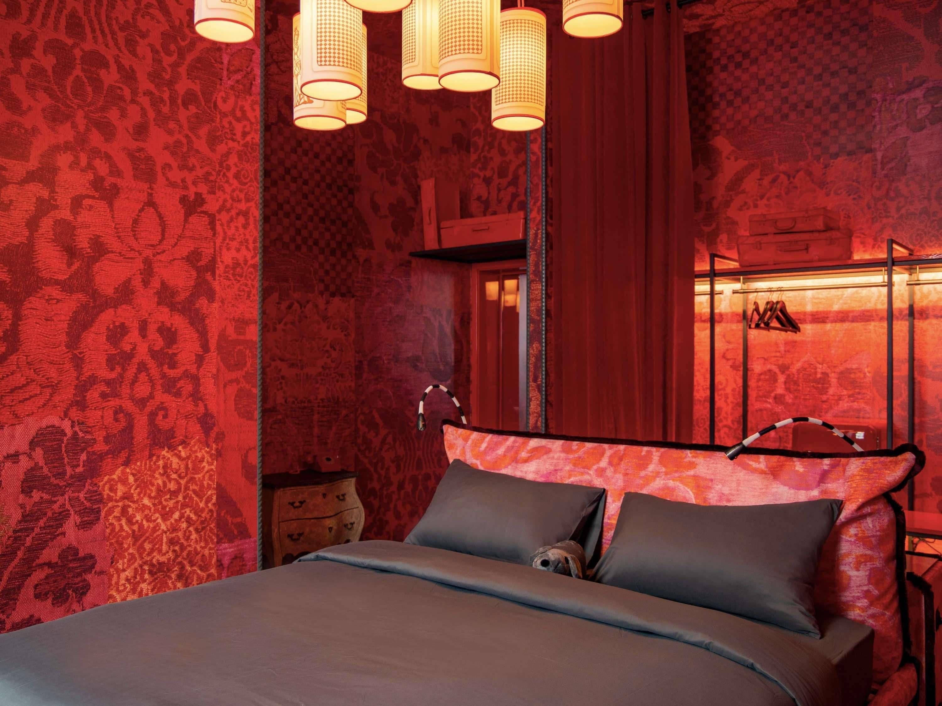 A bedroom with a bed, patterned wallpaper, and hanging lamps.