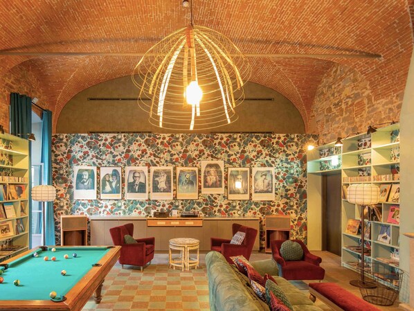 A cozy room with a pool table, red chairs, a sofa, and a wall adorned with framed pictures.