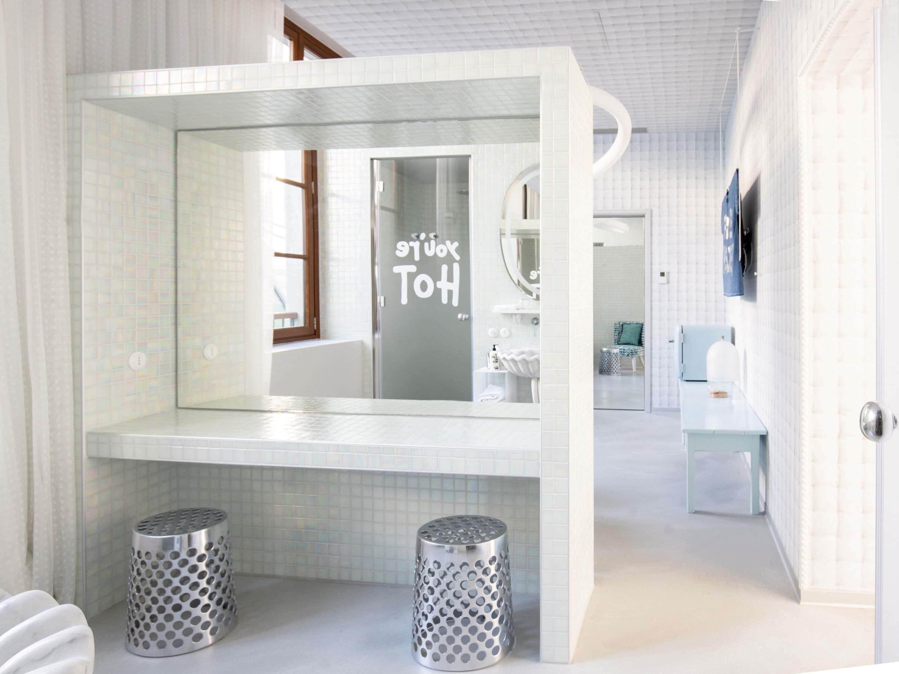 A modern bathroom with a glass partition, a sink, a mirror, and two metallic trash bins.