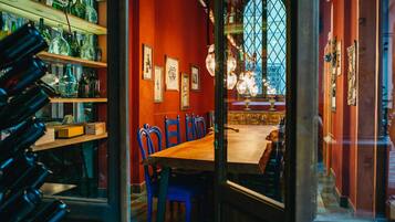 A dining area with a wooden table and blue chairs, shelves with bottles, and a large arched window with a view.
