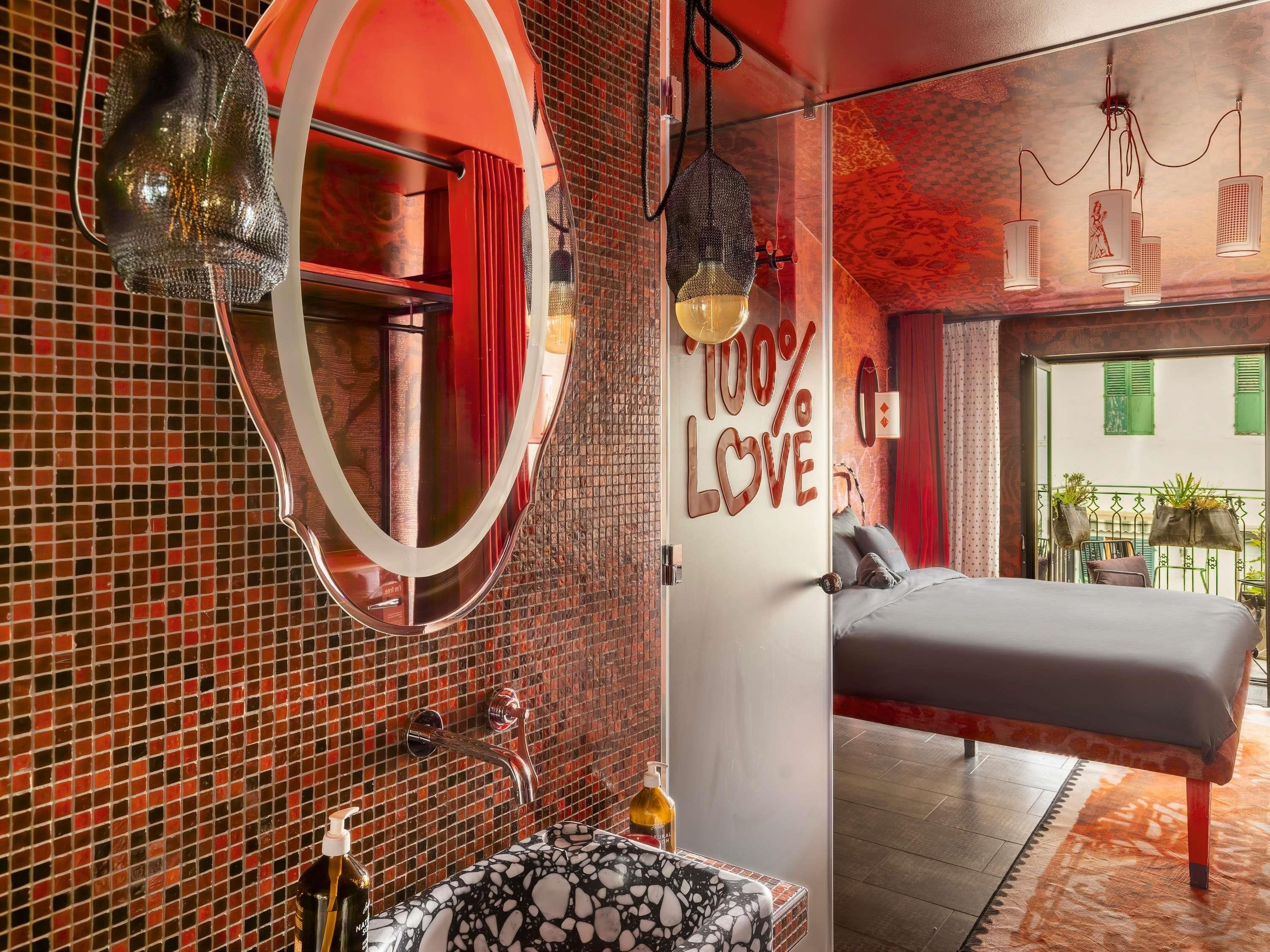 A modern bedroom with a large mirror, a bed, and a bathroom with a mosaic tile wall.