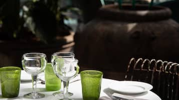 A table set with green glasses and a white plate, with a metal chair and a large pot in the background.