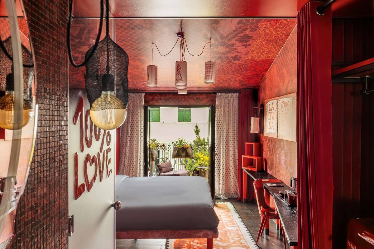 Une chambre à coucher avec un lit, un bureau et une chaise, un mur rouge et une fenêtre donnant sur un paysage verdoyant.