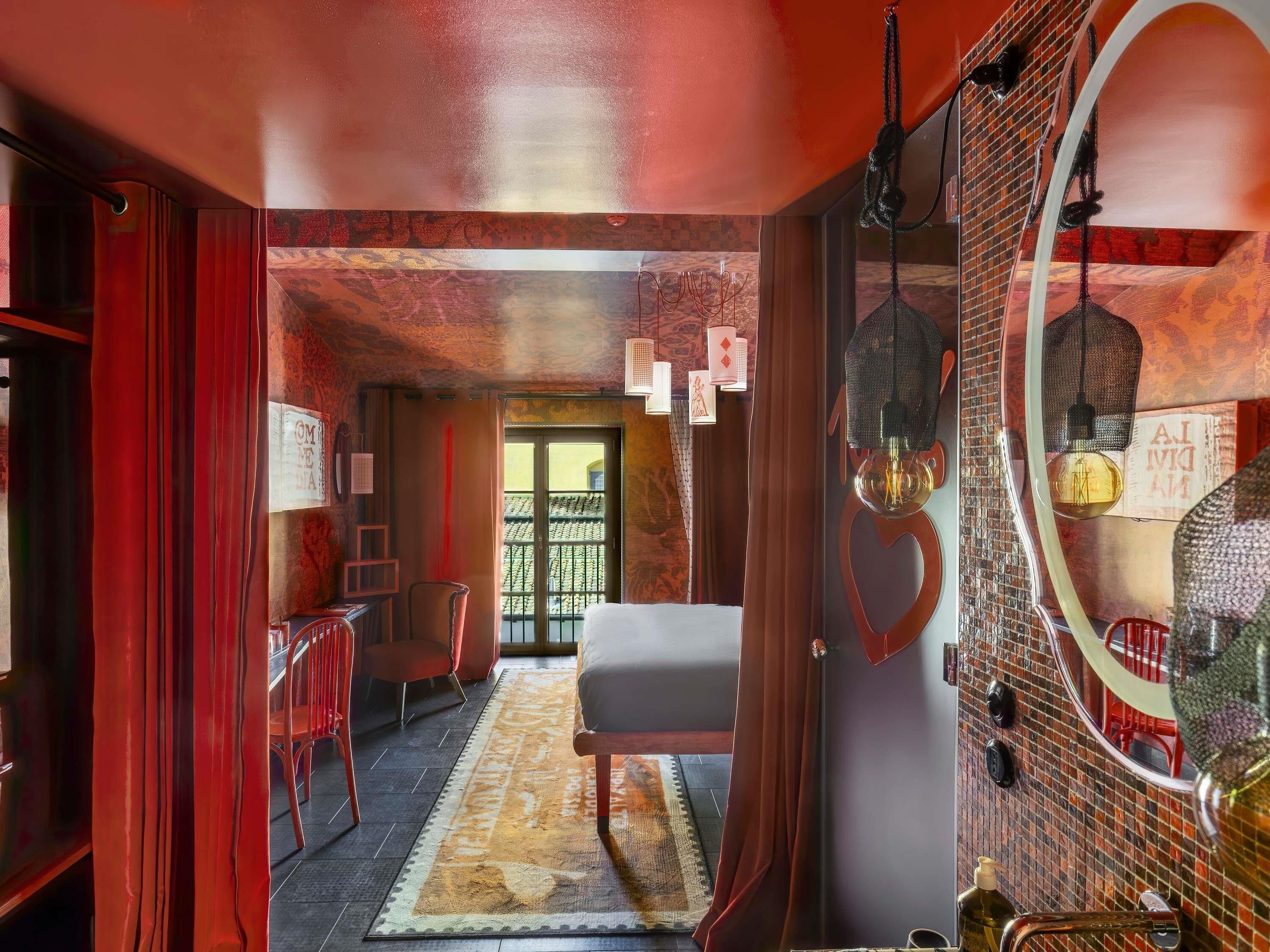 A room with a bed, a mirror, a red chair, a table, and a patterned rug.